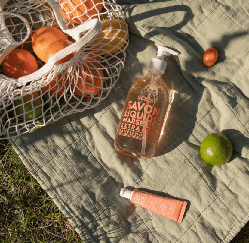 Bottle of Savon Liquide Marseillais Extra on a textured surface with oranges and a lime.