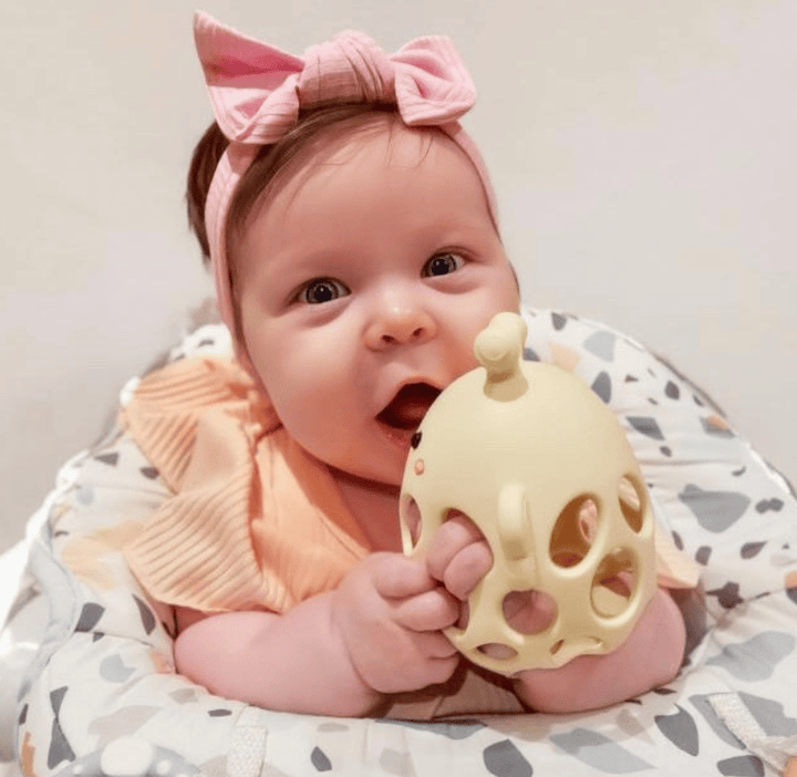 Baby holding a yellow teething toy with a pink bow headband
