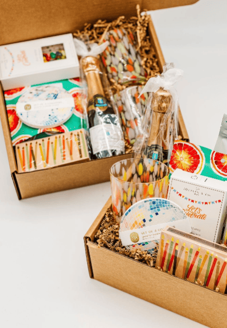 Gift box with champagne, snacks, and decorative items on a white surface