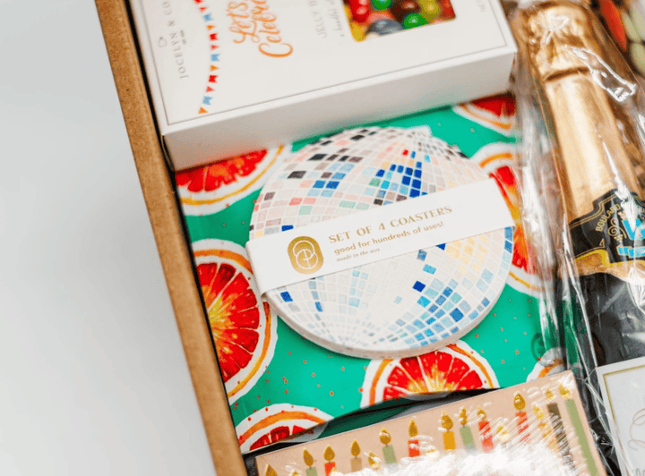 Set of coasters with colorful design on a box, accompanied by a bottle and packaging.