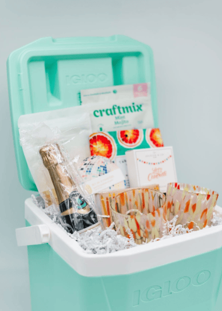 Teal Igloo cooler with ice and party supplies on a light gray background