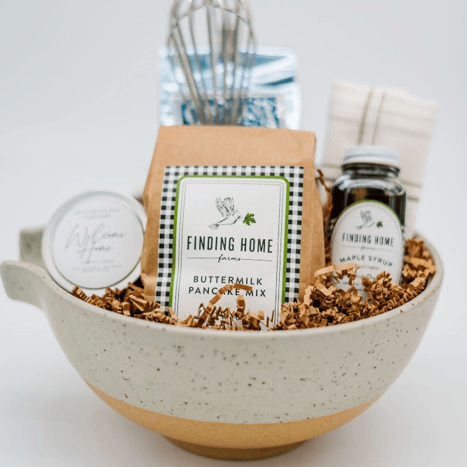Bowl with pancake mix, syrup, and other items labeled 'Finding Home' on a light background