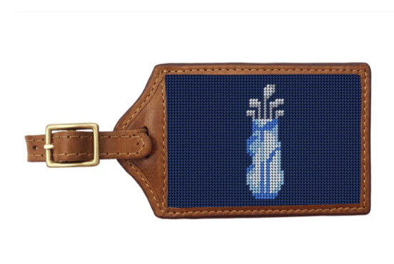 Luggage tag with needlepoint design of a golf bag and club on a blue background, attached to brown leather strap.