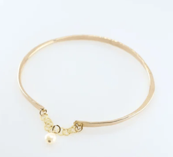 Gold bangle bracelet with safety chain and pearl accent on a white background