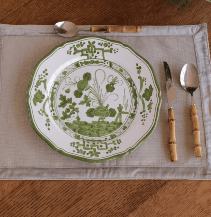 A green and white patterned melamine plate is set on a beige placemat with a bamboo-handled spoon, knife, and spoon on a wooden table.