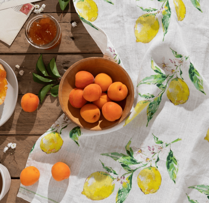 Wooden bowl of apricots on a table with a lemon-patterned tablecloth.