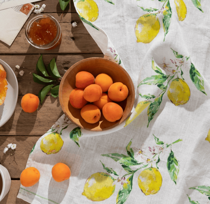 Wooden bowl of apricots on a table with a lemon-patterned tablecloth.