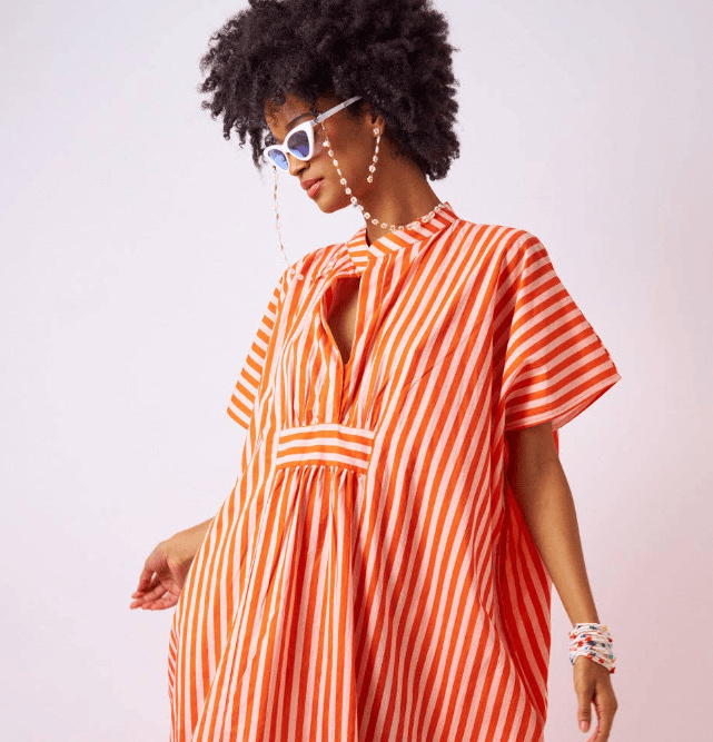 Woman wearing an orange and white striped dress against a plain background