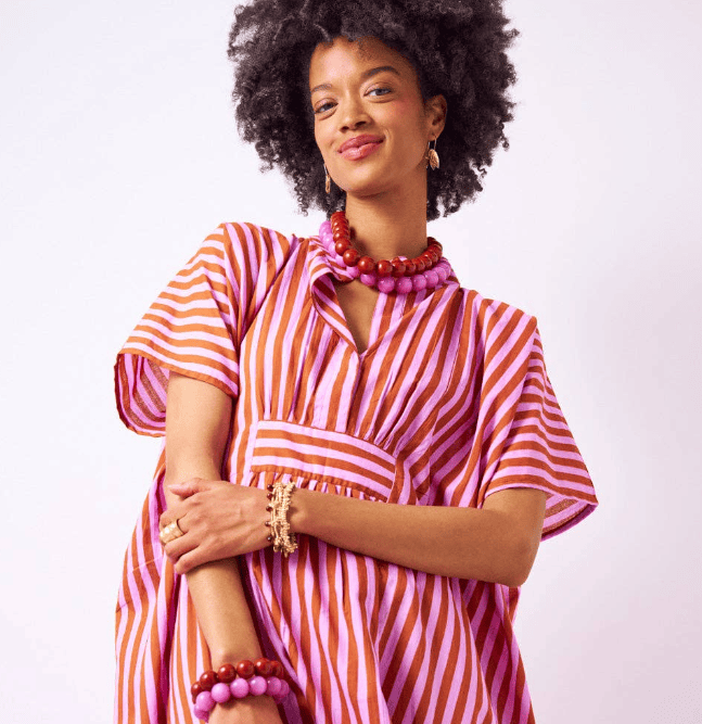 Woman wearing a pink and orange striped dress with jewelry on a white background