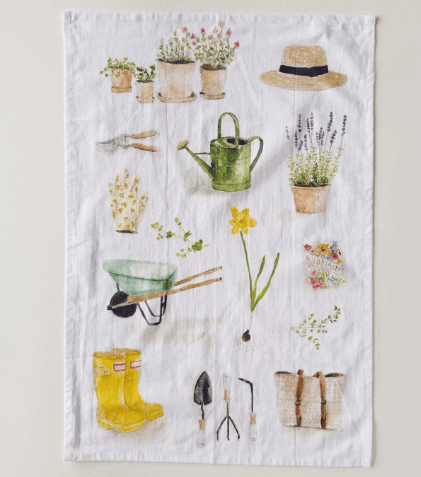 Gardening-themed tea towel with illustrations of plants, tools, and boots on a white background.