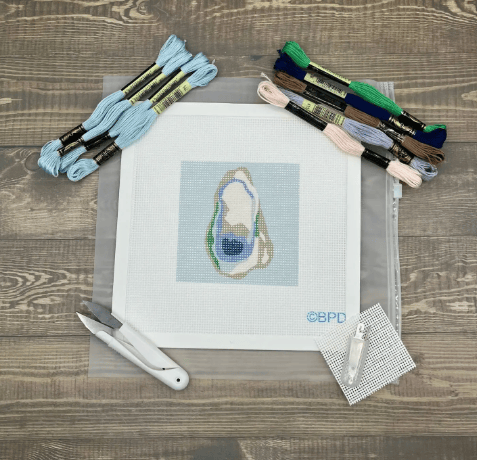 Cross-stitch kit with oyster design on fabric, threads, and tools on a wooden surface