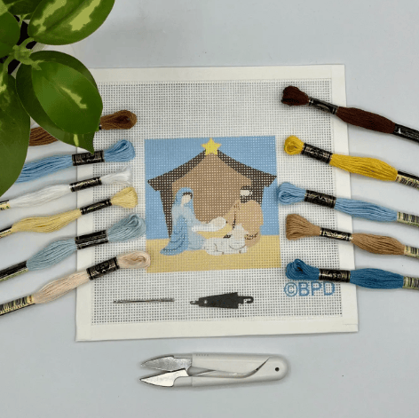 Embroidery kit with a Nativity scene design, threads, and tools on a gray surface.