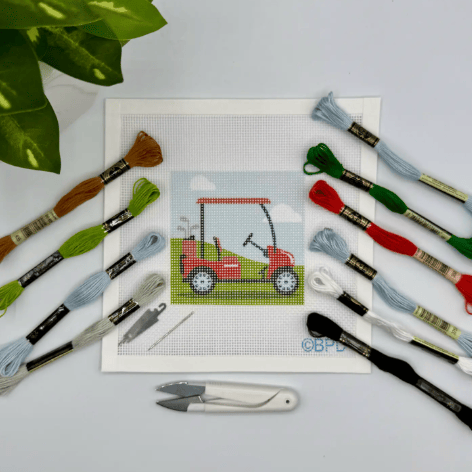 Cross-stitch kit with a red golf cart design, threads, and tools on a light gray background.
