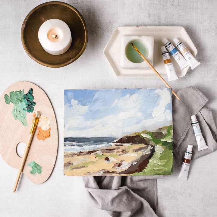 Painting of a coastal scene with art supplies on a gray surface