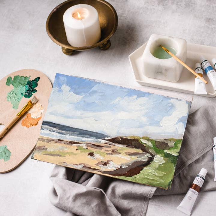 Painting of a landscape with art supplies on a gray surface