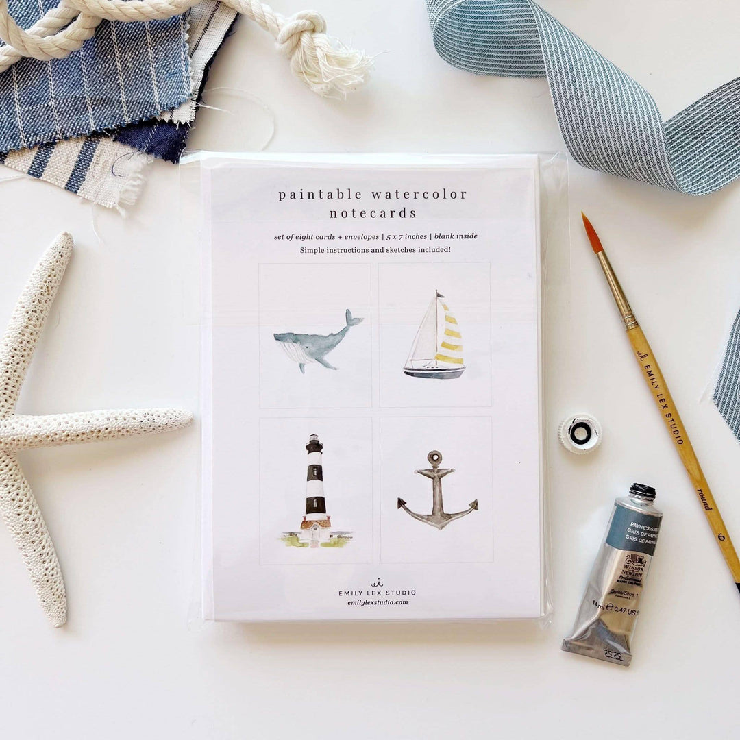 Paintable watercolor notecards with nautical illustrations on a white surface with art supplies.