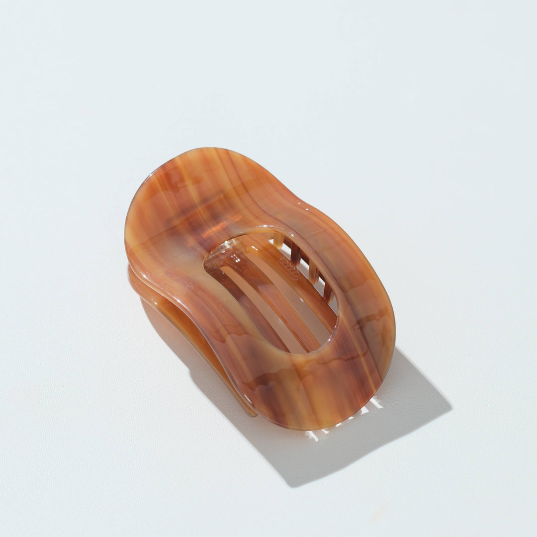 A translucent tortoiseshell hair claw clip in warm amber-brown tones, photographed on a clean white background with a soft shadow.
