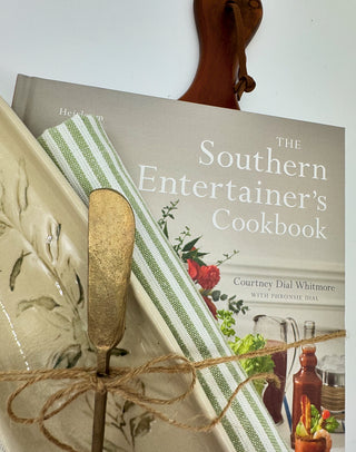 What a great housewarming gift: The Southern Entertainer's Cookbook, ceramic olive tray, brass spreading knife, green and white heavy duty kitchen towel and wooden charcuterie board. 