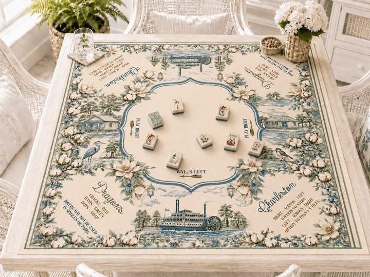 Mahjong mat with floral illustrations and printed text, set on a white wicker table in a bright room with white chairs and flowers.