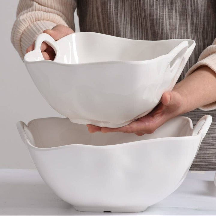 Person holding a white ceramic bowl with another bowl underneath on a light background