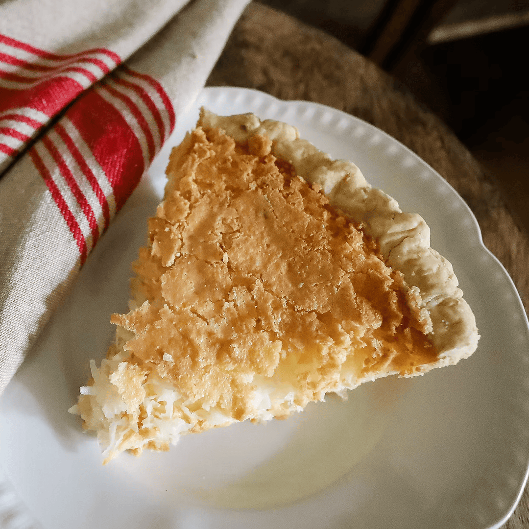 Slice of coconut custard pie on a white plate with a red and white striped towel