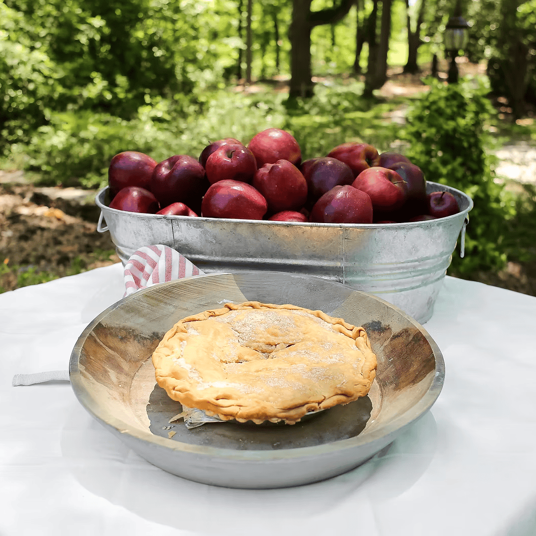 Pie on a metal plate with a bucket of apples in an orchard setting