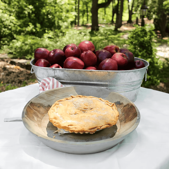 Pie on a metal plate with a bucket of apples in an orchard setting