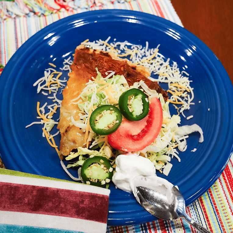 Blue plate with a taco pie and a spoon on a colorful striped tablecloth.