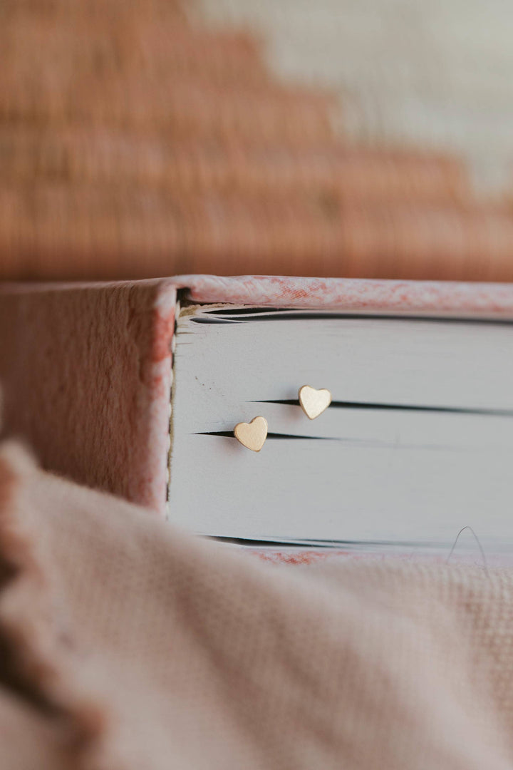 Heart-shaped gold earrings on a white surface with a blurred background