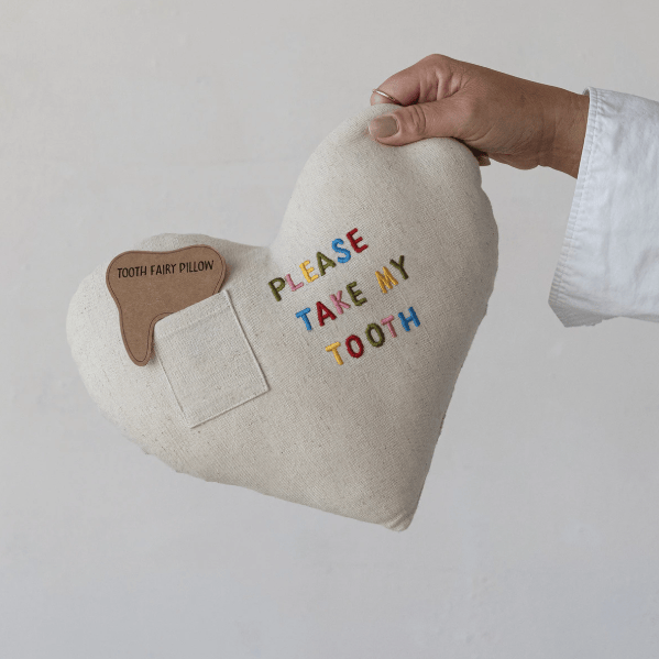 Hand holding a pillow with 'Please Take My Tooth' text on a plain background