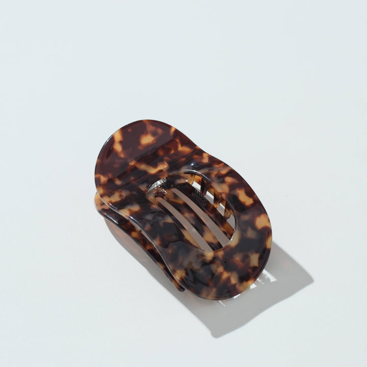 A tortoiseshell hair claw clip with a glossy amber-brown and black mottled pattern, shown on a clean white background with a soft shadow.