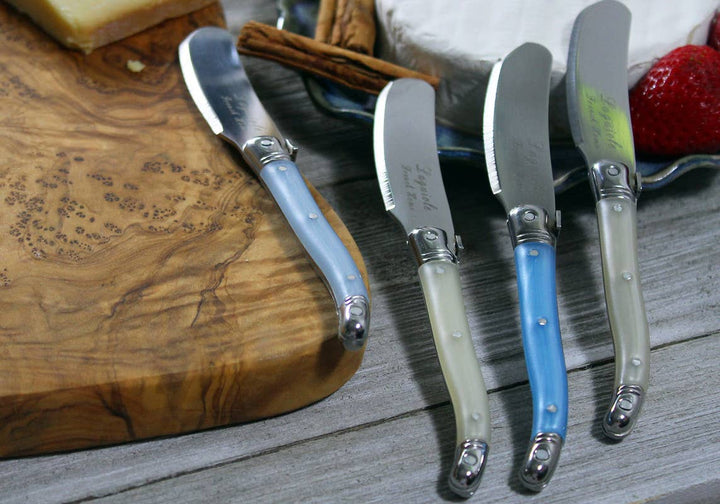 Set of four cheese spreaders with different shades of blue or cream handles on a wooden board.