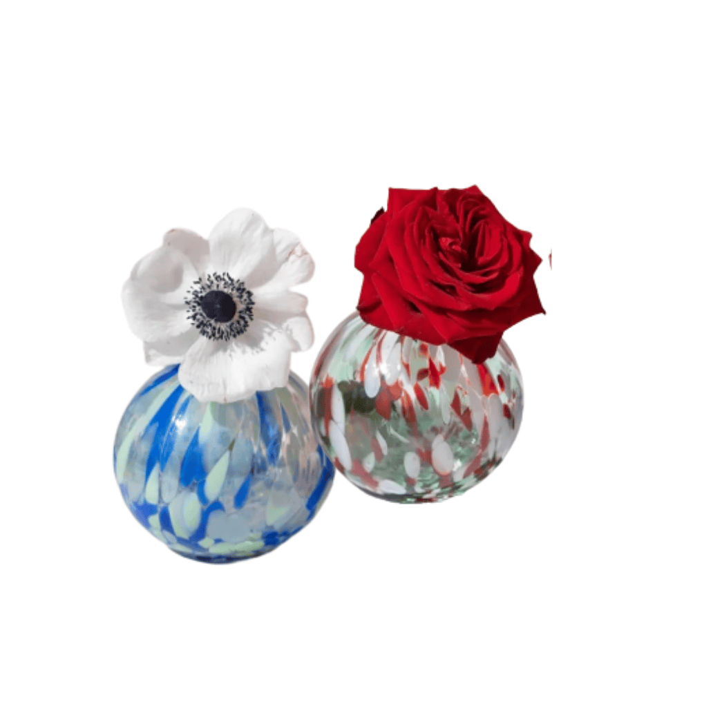 Two decorative glass vases on a plain white background, one with a blue and white marbled body and a white flower with a dark center, and the other with a red, white, and green marbled body and a red rose.