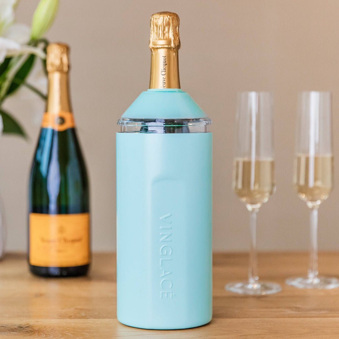 Light blue wine bottle cooler with champagne bottle and glasses on a wooden surface