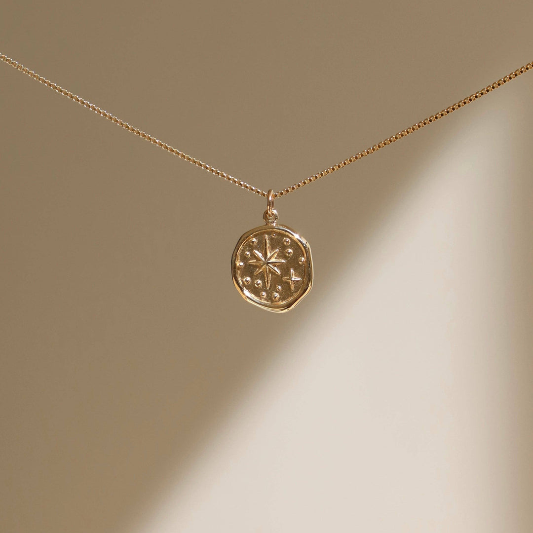 Gold necklace with a round pendant on a beige background