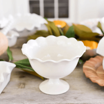 White footed trifle bowl on a table with greenery and other dishes.