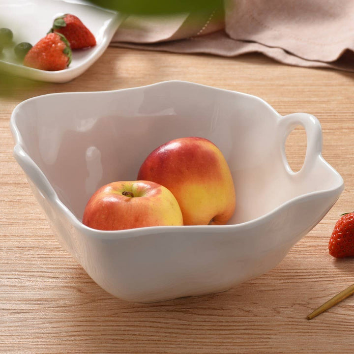 White fruit bowl with apples and a strawberry on a wooden table