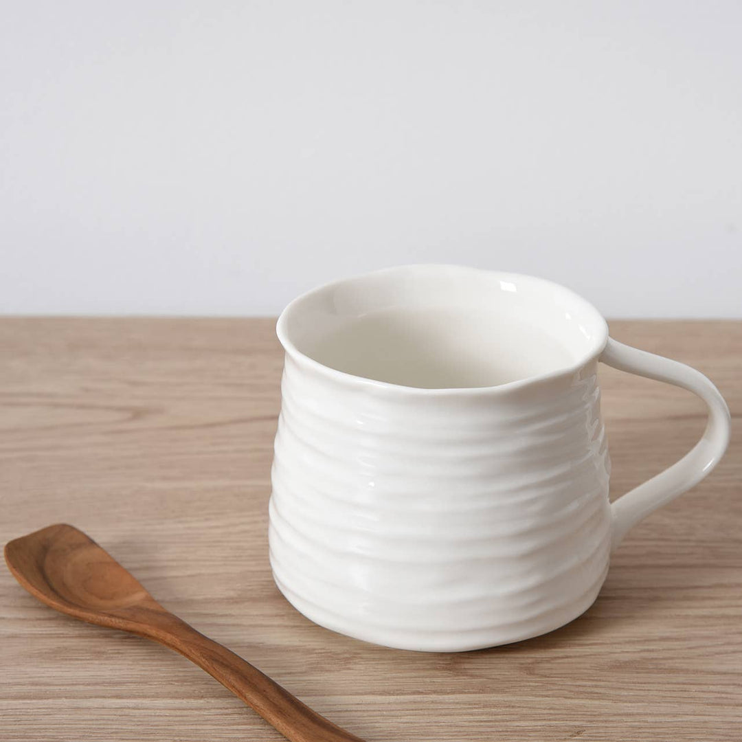 White ceramic mug on a wooden surface with a wooden spoon