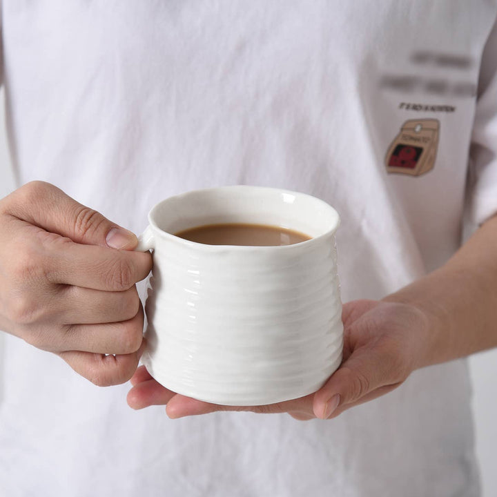 Person holding a white mug with a beverage against a plain background