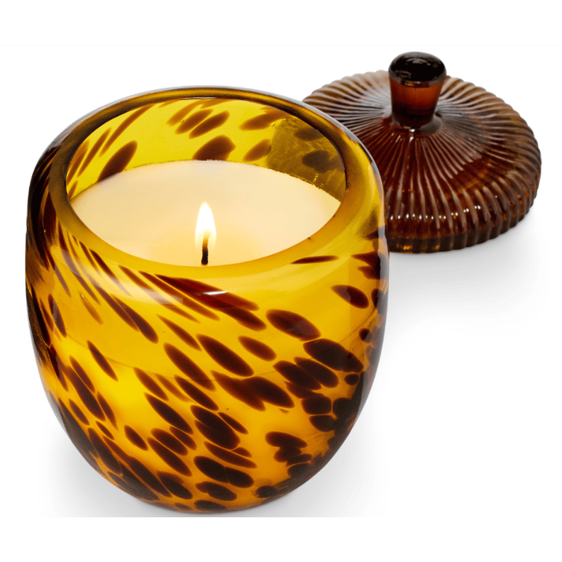 A lit candle in a round amber glass jar with a dark tortoiseshell pattern, shown with its matching ribbed lid on a white background.