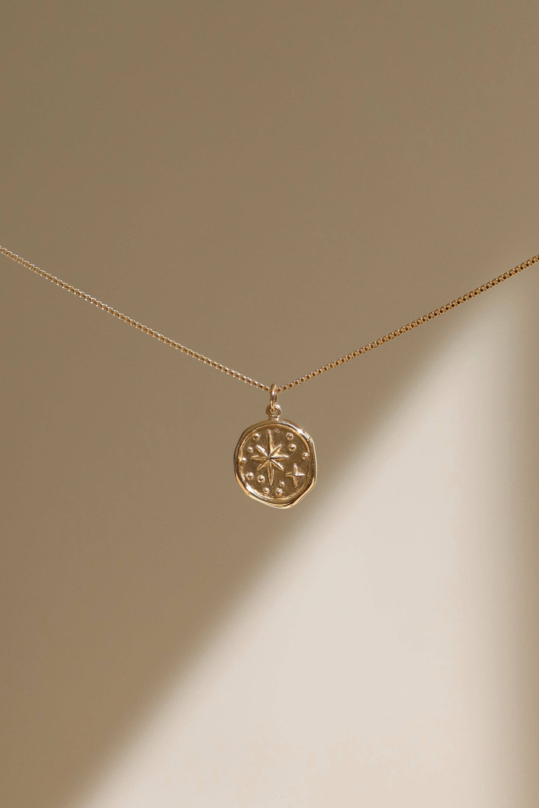 Gold necklace with a round pendant on a beige background