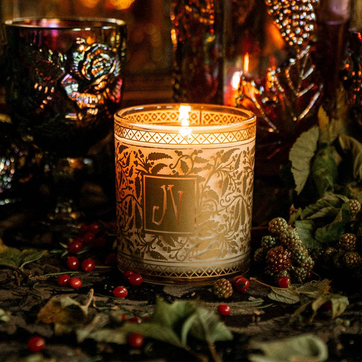 Decorative candle with intricate design and 'ELV' logo, surrounded by berries and leaves.