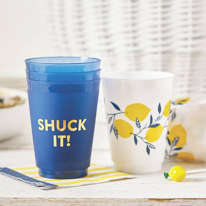 Blue cup with 'SHUCK IT!' text and white cup with lemon design on a striped surface.