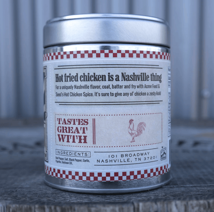 A cylindrical metal spice tin with a silver lid and a white label featuring red and black text, placed on a weathered wooden surface against a corrugated metal backdrop.