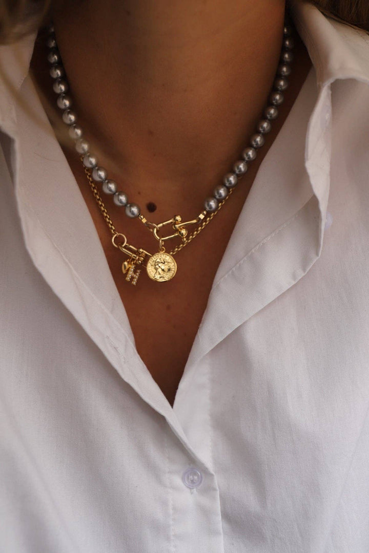 Pearl necklace with gold charm worn by a person in a white shirt