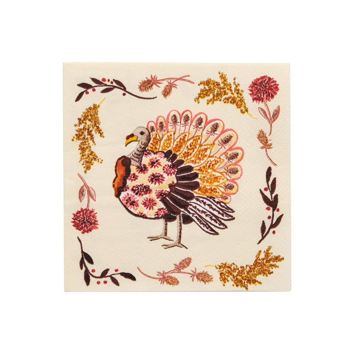 A square cream-colored cocktail napkin featuring a detailed illustration of a turkey surrounded by autumn leaves and berries in red, gold, and brown.
