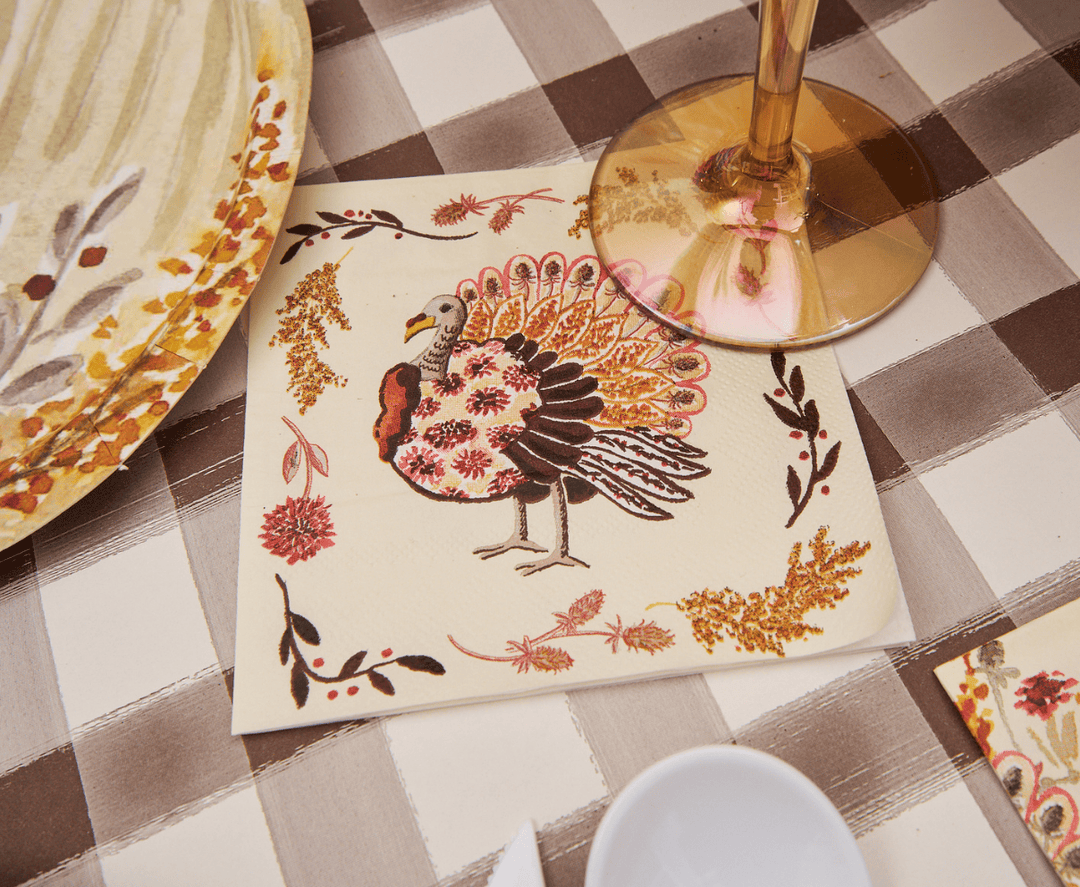 Napkin with a turkey design on a checkered tablecloth with a glass of wine.
