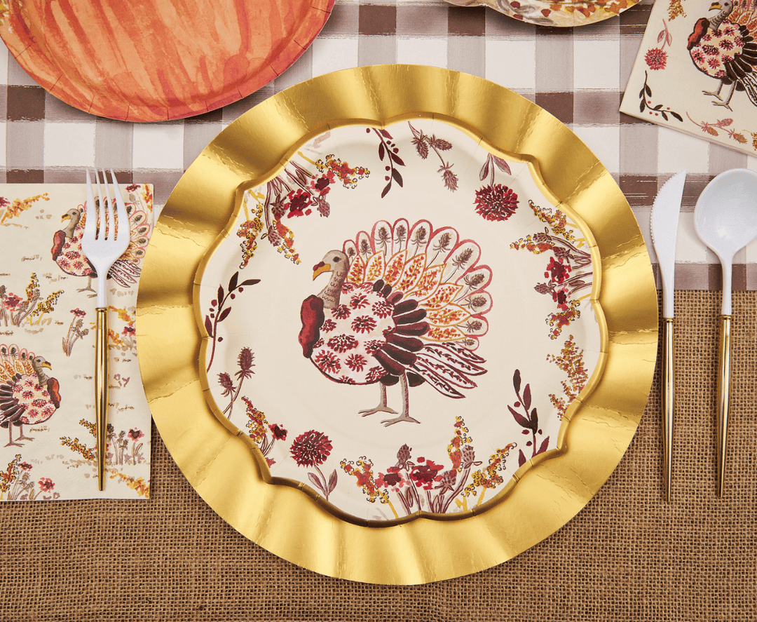 Decorative plate with a turkey design on a gold-rimmed plate, set on a table with a checkered tablecloth.