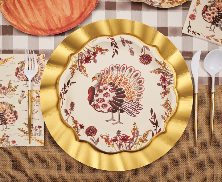 Decorative plate with a turkey design on a gold-rimmed plate, set on a table with a checkered tablecloth.
