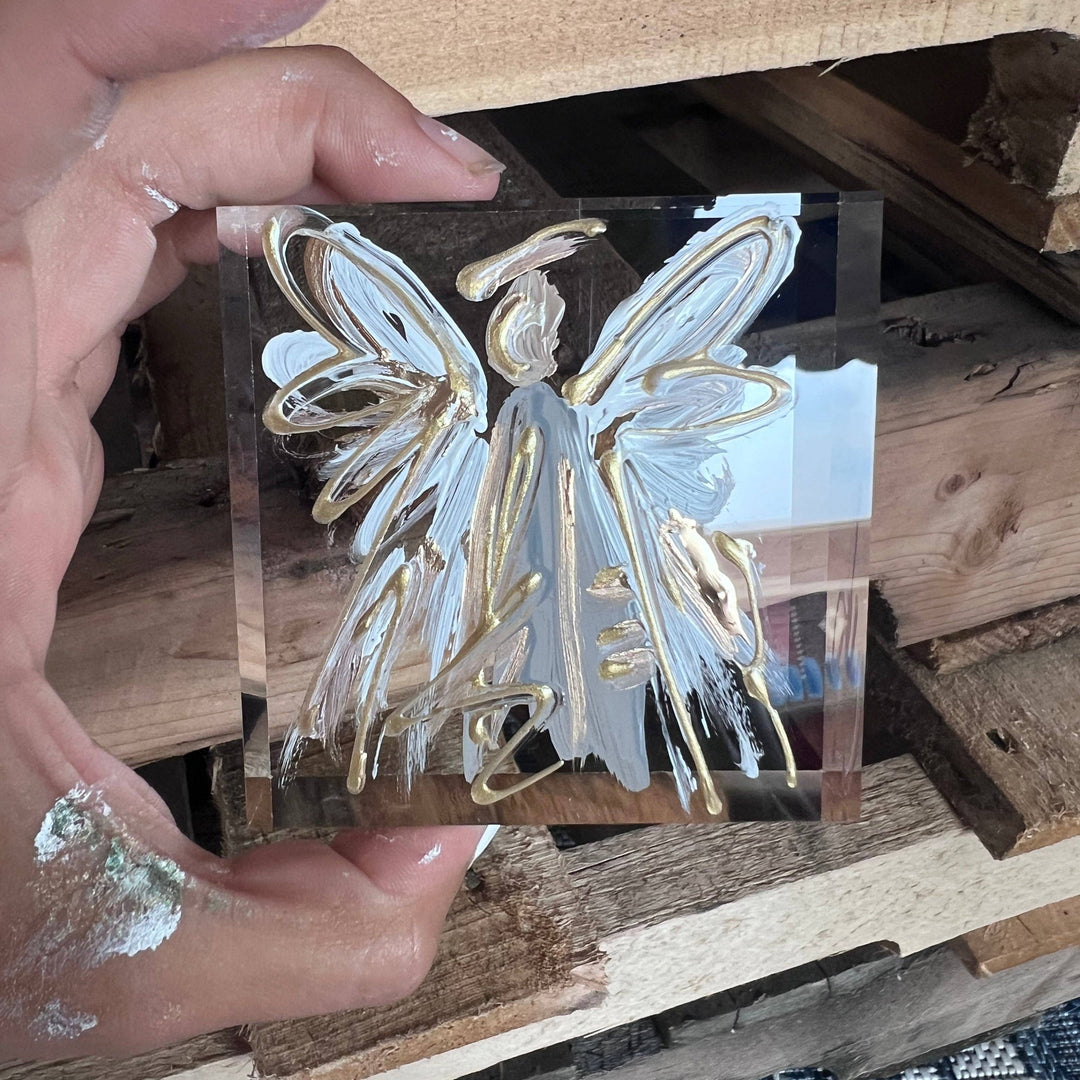 Hand holding a clear acrylic block with blue and gold angel design.